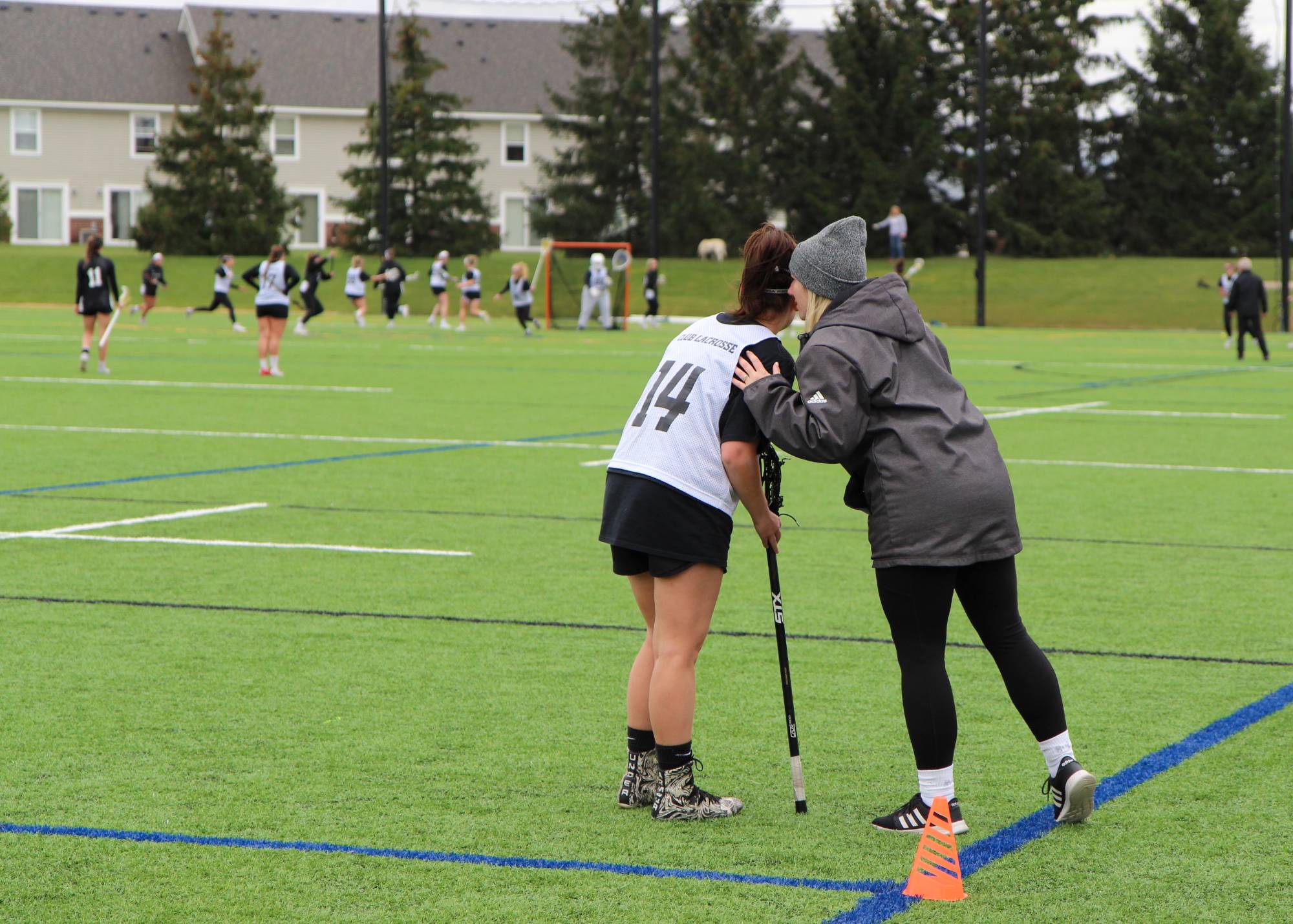coach leaning in from the sideline to talk to a women's lacrosse player